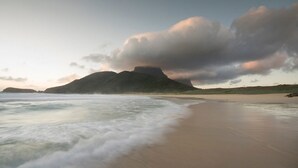 Une plage avec une montagne en arrière-plan et des vagues qui se rapprochent du rivage.