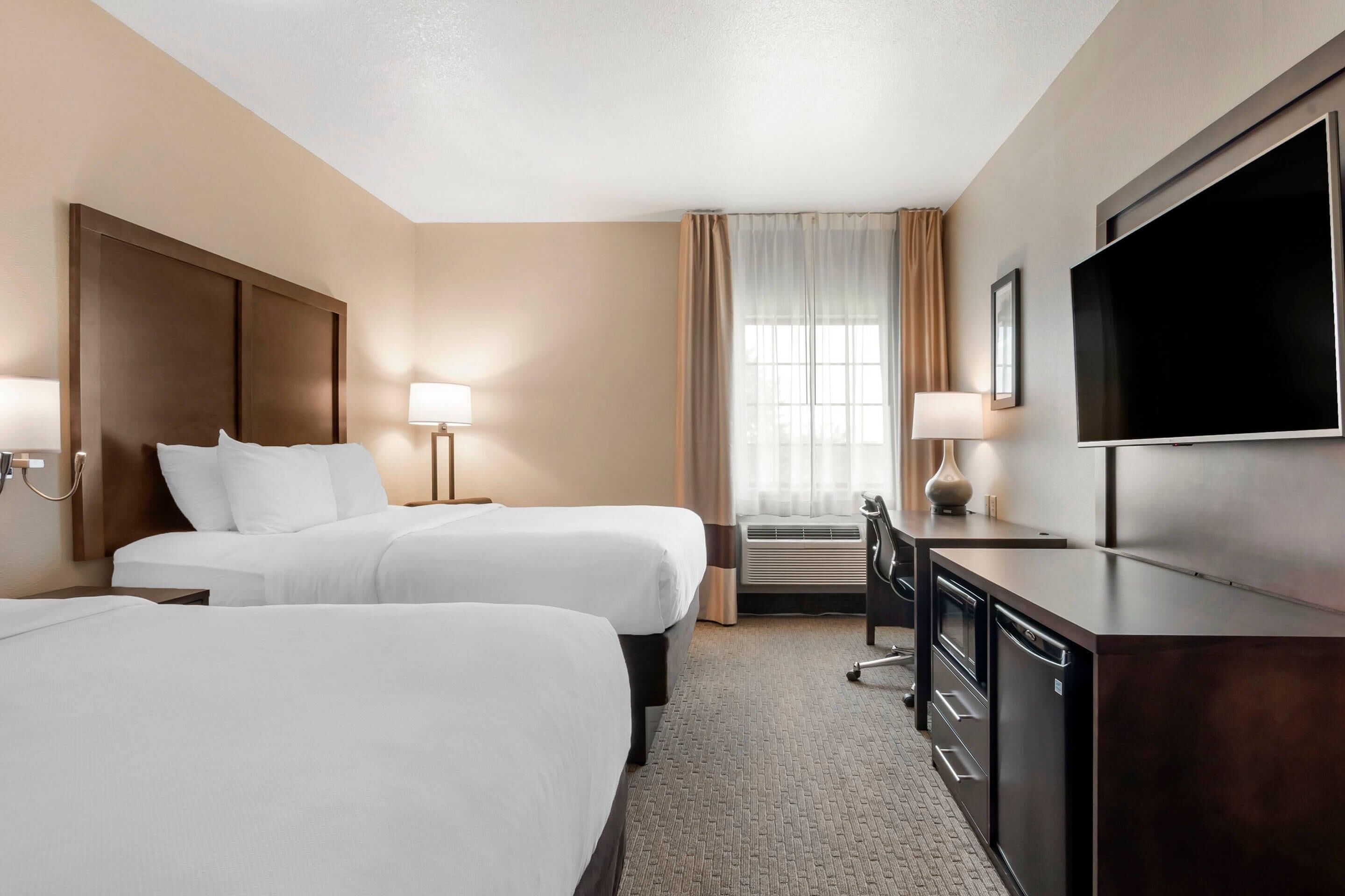 A hotel room with two beds, a TV, a desk, and a window with curtains.