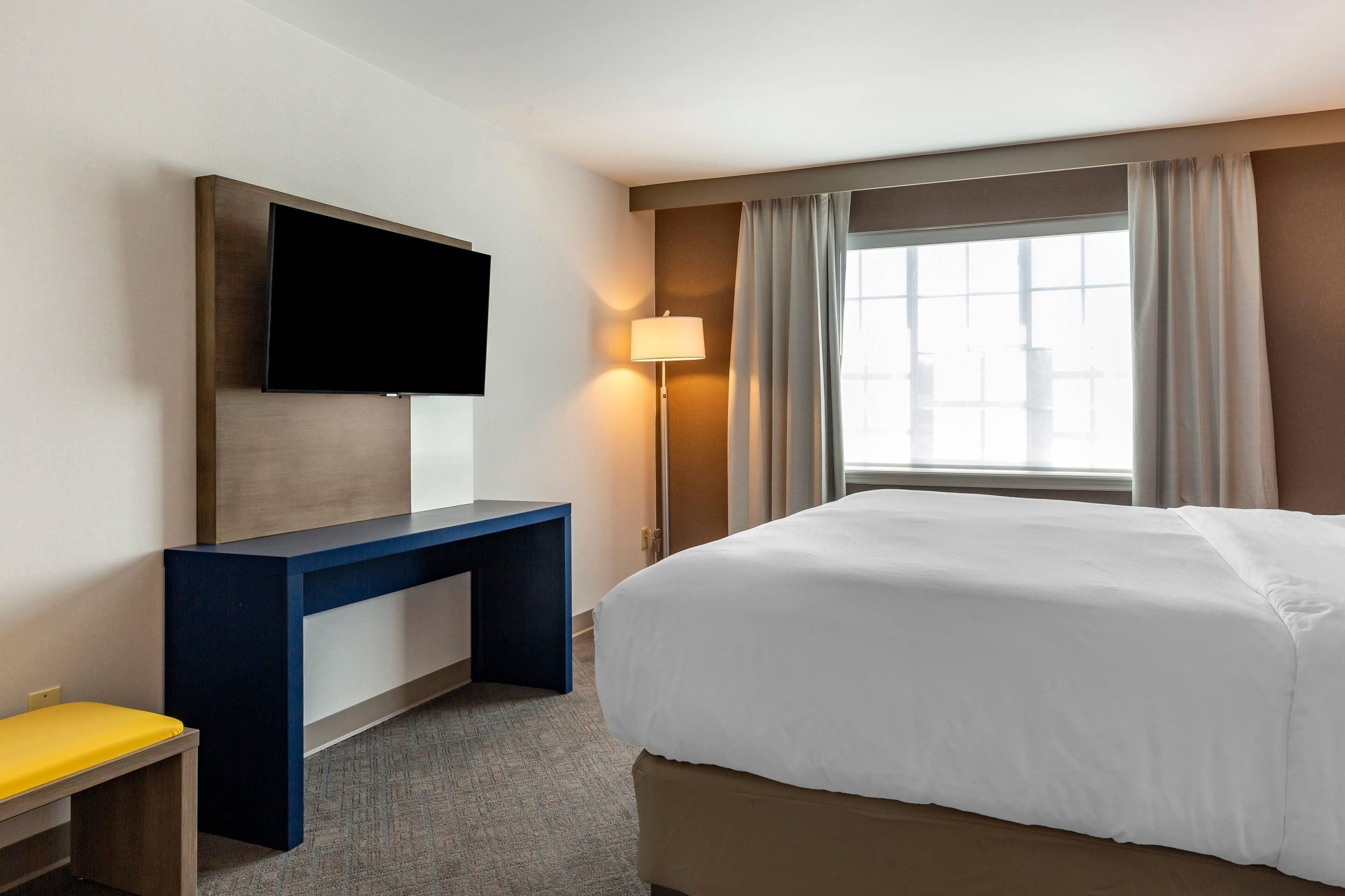 Une chambre d’hôtel avec un lit, un bureau, une télévision et une fenêtre avec des rideaux.