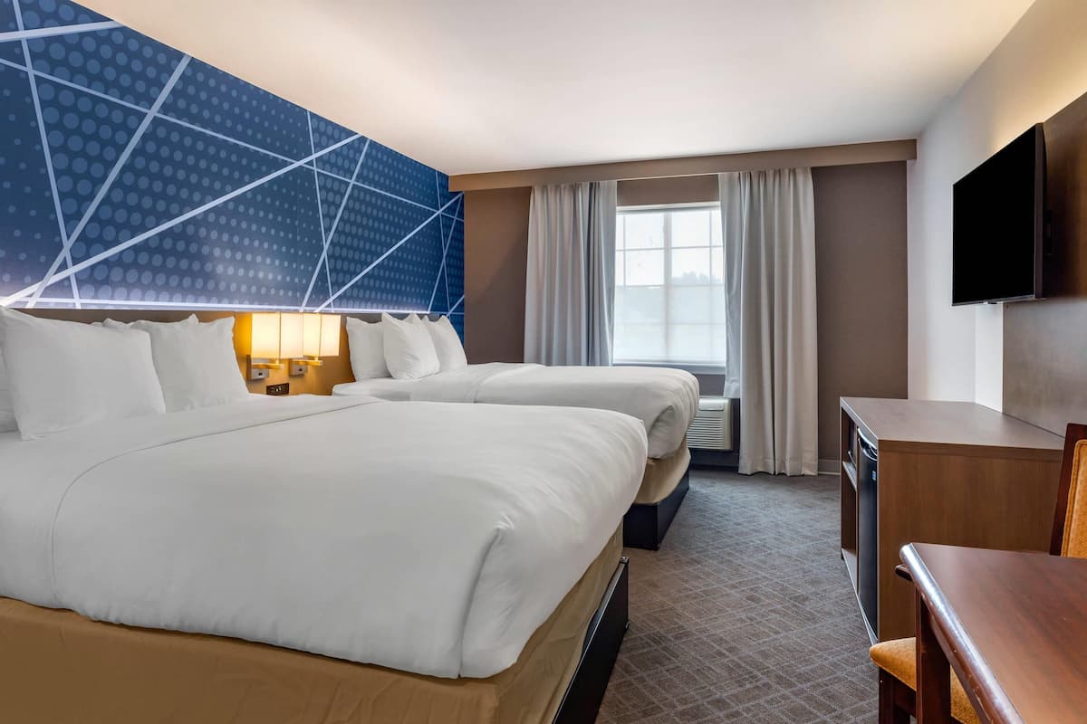 A hotel room with two beds, a desk, a television, and a large window with curtains.