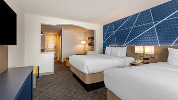 A hotel room with two beds, a desk, a TV, and a large wall with a geometric pattern.