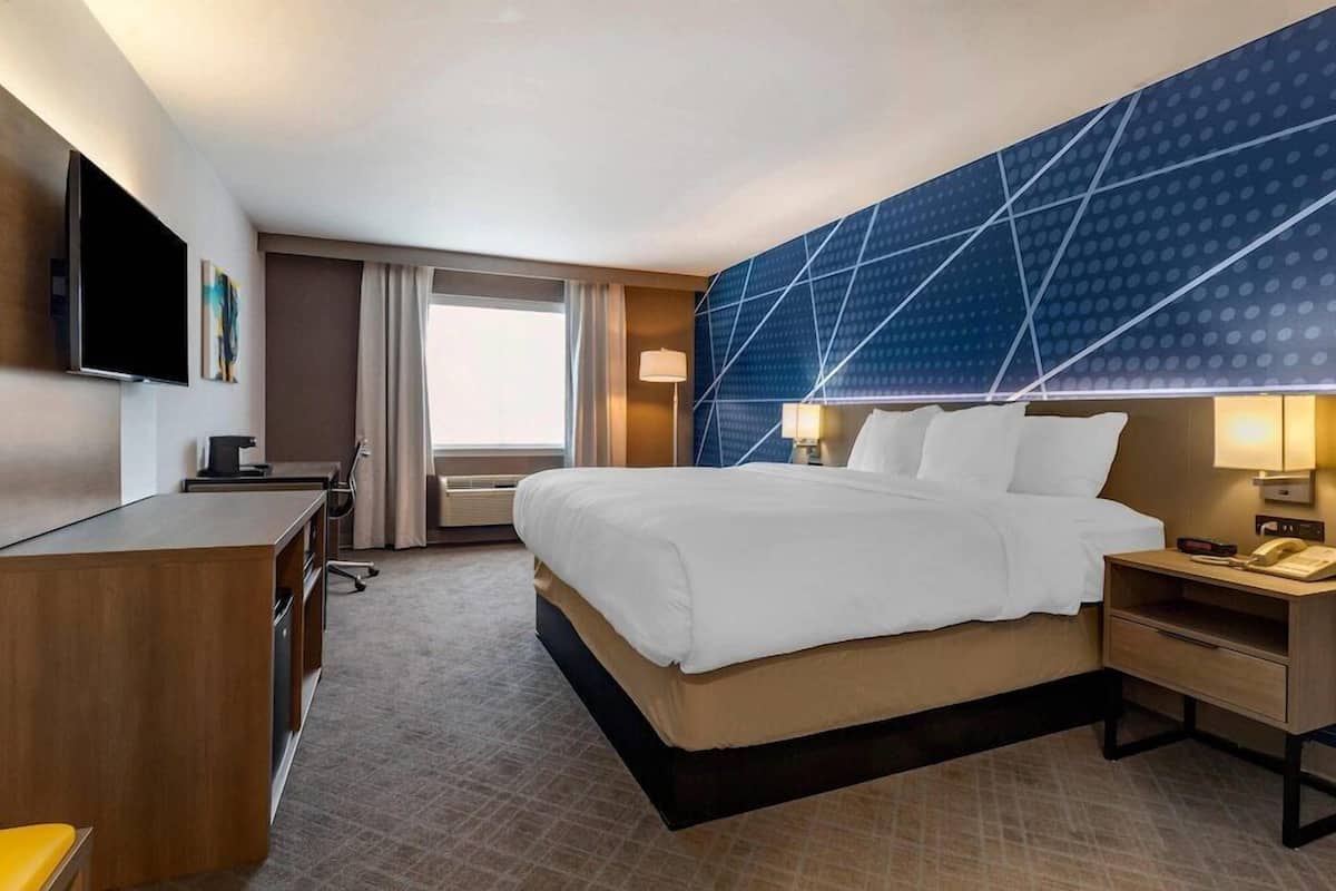 A hotel room with a bed, desk, TV, and a large window.
