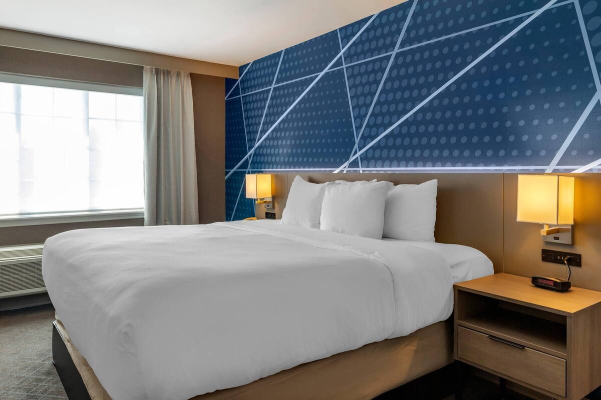 A hotel room with a large bed, two bedside lamps, a nightstand, and a window with curtains.