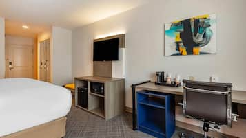 A hotel room with a bed, desk, chair, TV, and artwork.