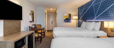 A hotel room with two beds, a desk with a microwave, a TV, and artwork on the walls.