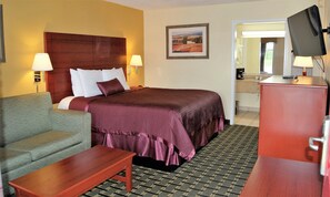 A hotel room with a bed, a desk, a chair, a television, and a bathroom visible through an open door.