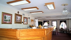 Un espace d’accueil avec un comptoir de réception en bois, des tableaux encadrés au mur, un lustre et une vue sur l’extérieur grâce à de grandes fenêtres.