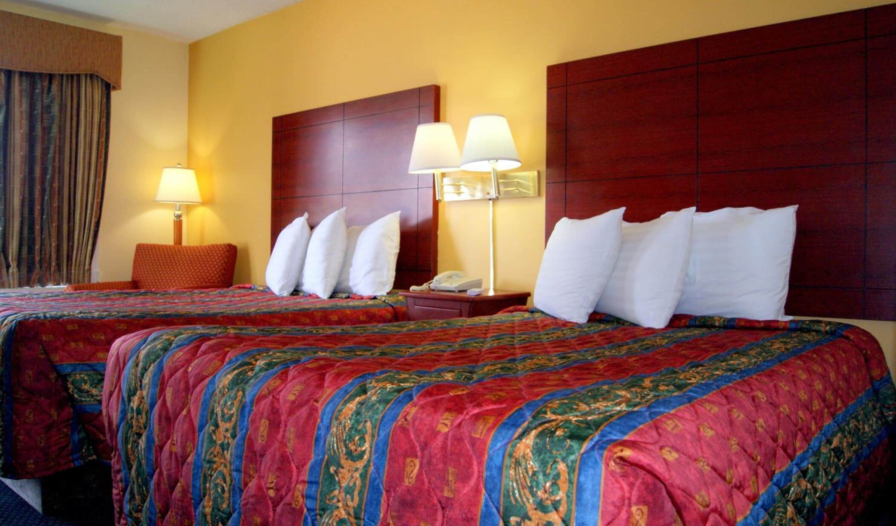 Habitación de hotel con dos camas, cada una con una colcha estampada en rojo y azul, cabeceros de madera y dos lámparas de noche.