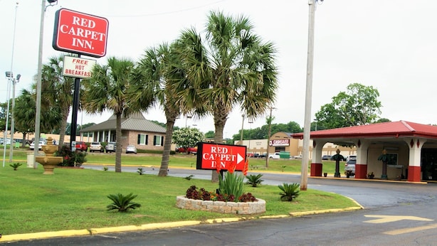 Un hôtel Red Carpet Inn avec un panneau indiquant que le petit-déjeuner chaud est offert gratuitement, un magasin Cash Saver à proximité et un espace de stationnement.