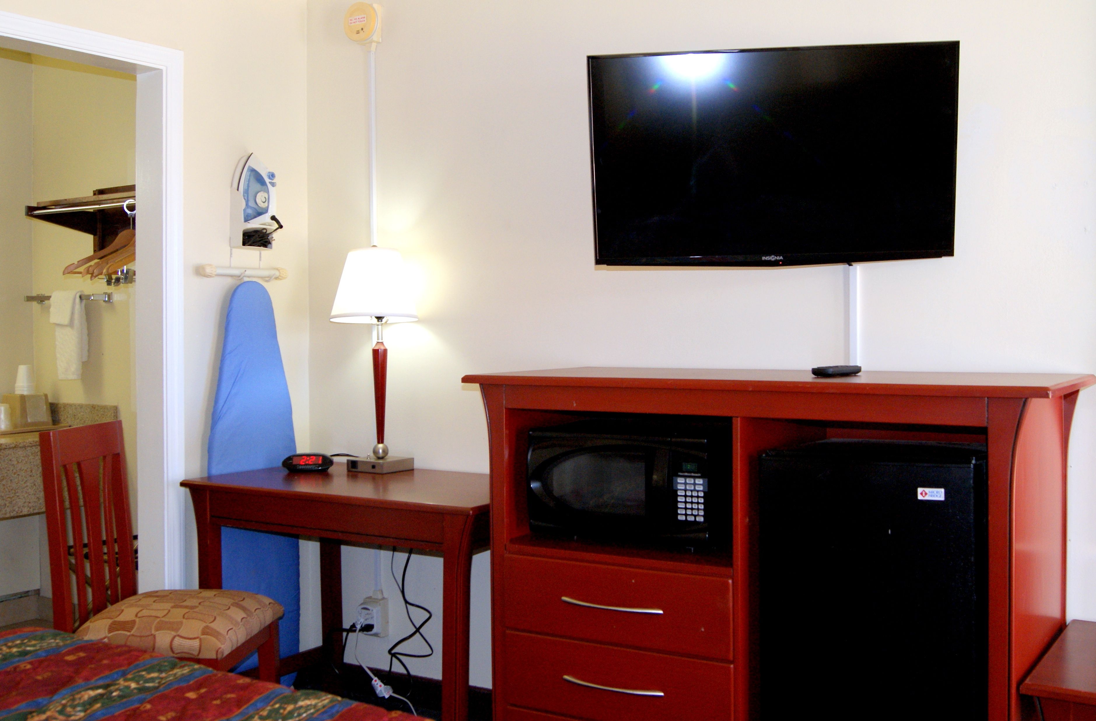 A hotel room with a TV, a microwave, a desk with a lamp, and a chair.