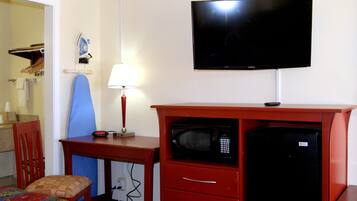 A hotel room with a TV, a microwave, a desk with a lamp, and a chair.