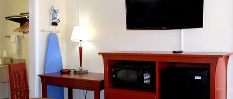 A hotel room with a TV, a microwave, a desk with a lamp, and a chair.