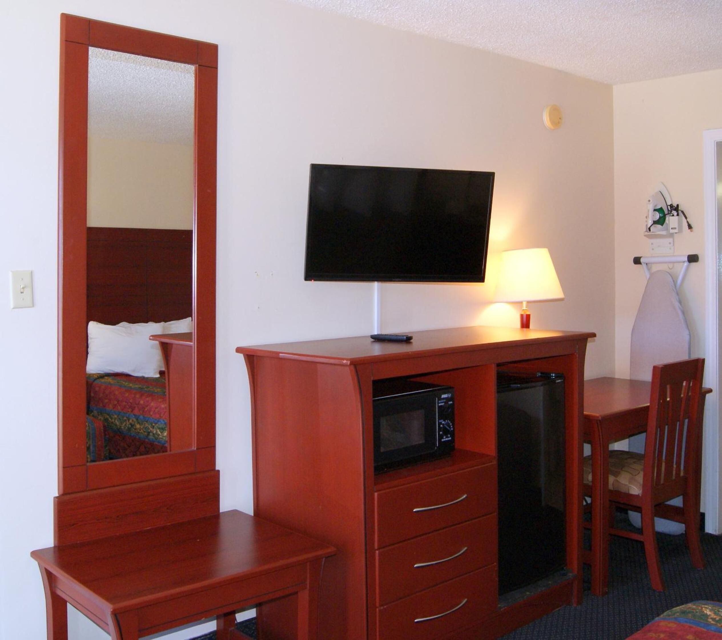 A hotel room with a wooden desk, a television, a microwave, a lamp, and a bed with a colorful blanket.