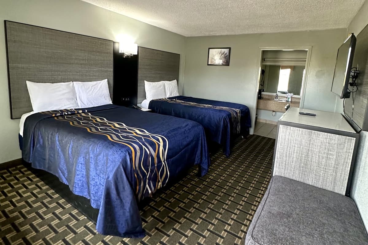 A hotel room with two beds, a desk, a chair, and a bathroom visible through an open door.