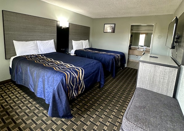 A hotel room with two beds, a desk, a chair, and a bathroom visible through an open door.