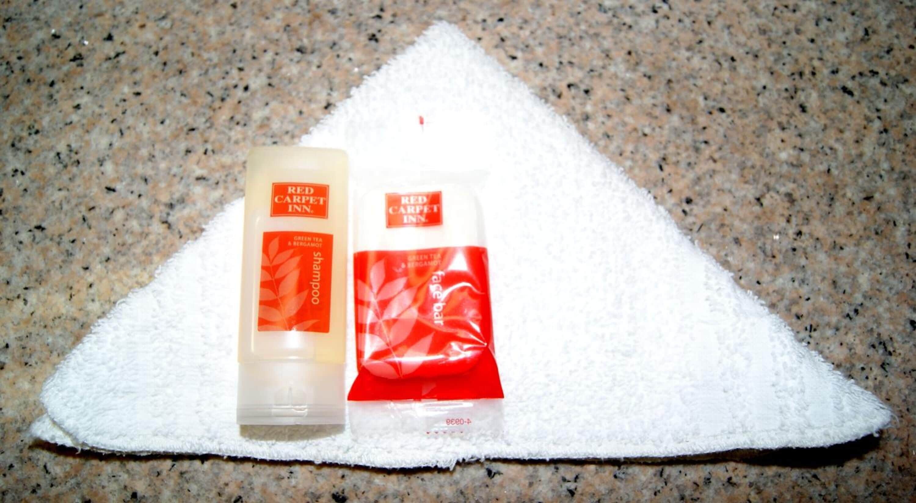 Two Red Carpet Inn shampoo bottles on a white towel.