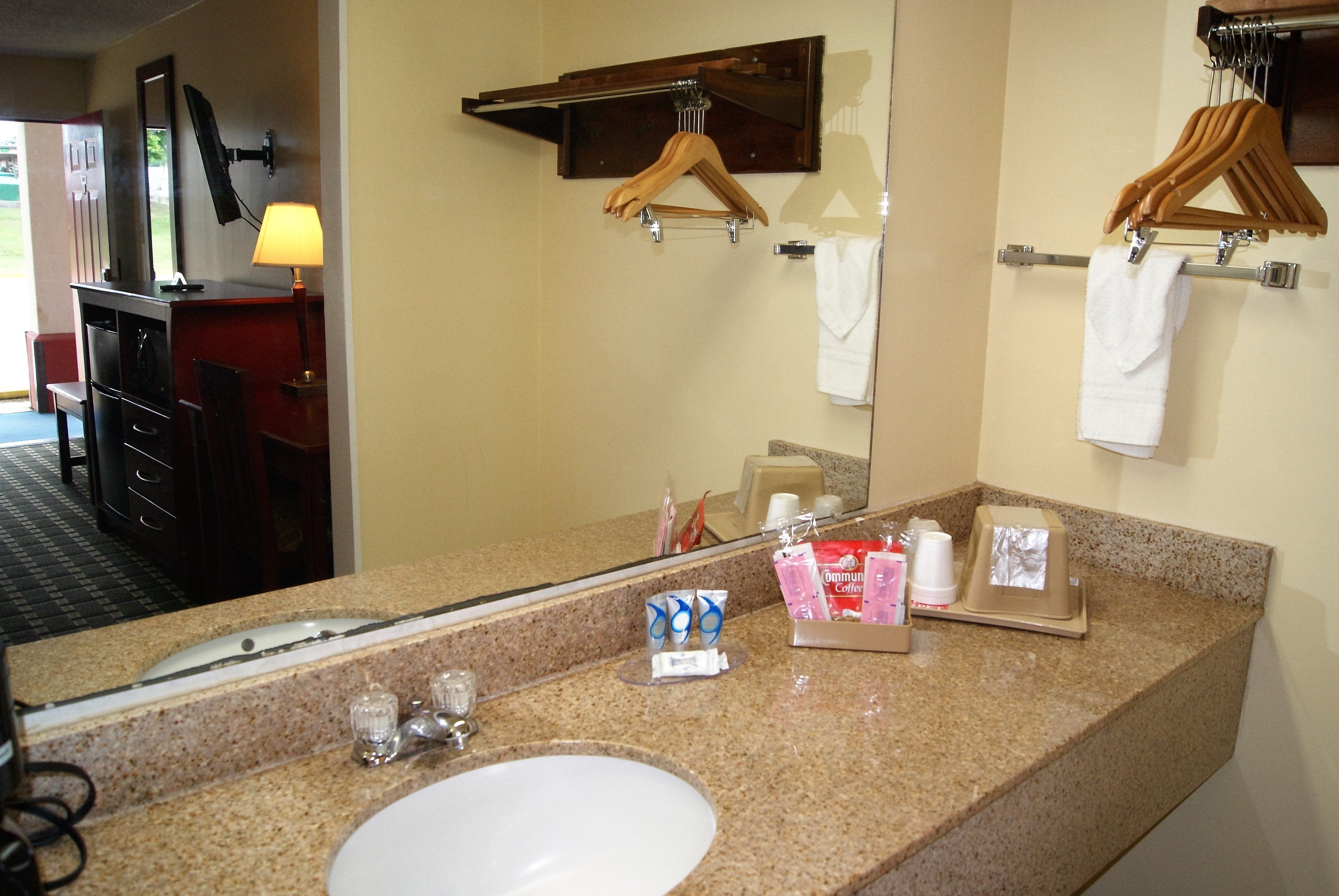 A hotel bathroom with a granite countertop, sink, mirror, towel rack, and a wooden hanger.