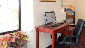 Un petit bureau avec un bureau, une chaise, un ordinateur portable, une plante en pot, un tableau encadré et une étagère remplie de magazines.