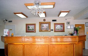 A reception desk with framed pictures on the wall, a chandelier, and ceiling lights.