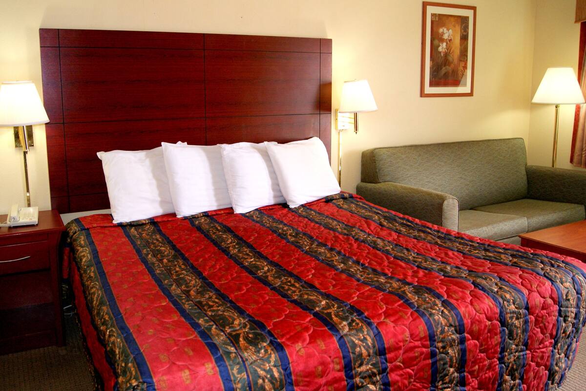 A hotel room with a large bed, a bedside table with a phone, two lamps, a green sofa, and a painting on the wall.