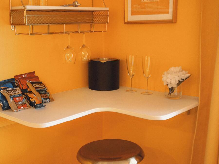 Eine Bar mit einer weißen Arbeitsplatte, einem Metallhocker und einem Bilderrahmen mit einem Champagnerglas.