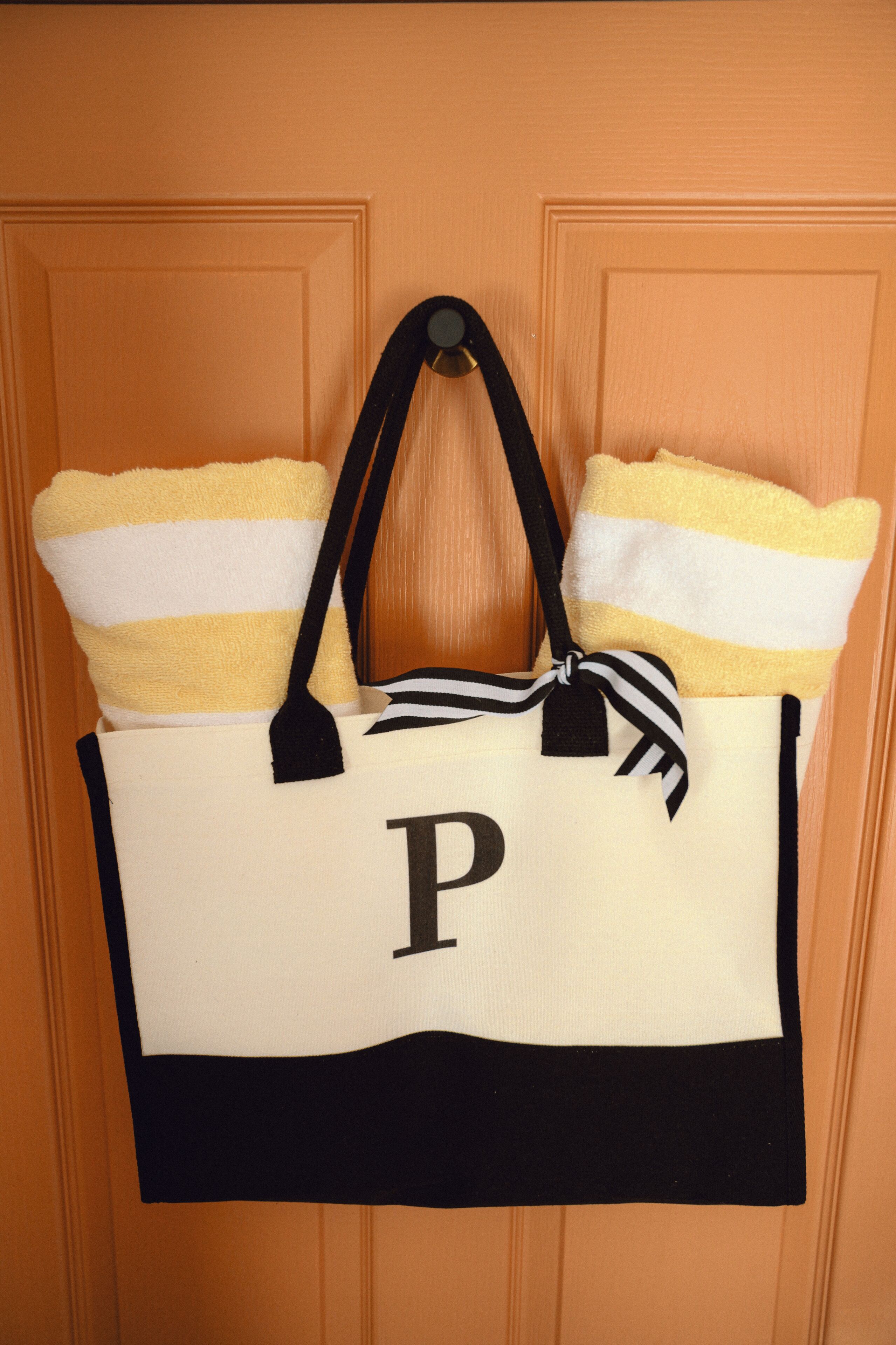 A white bag with a black handle and a black and white striped towel, hanging on a wooden door.