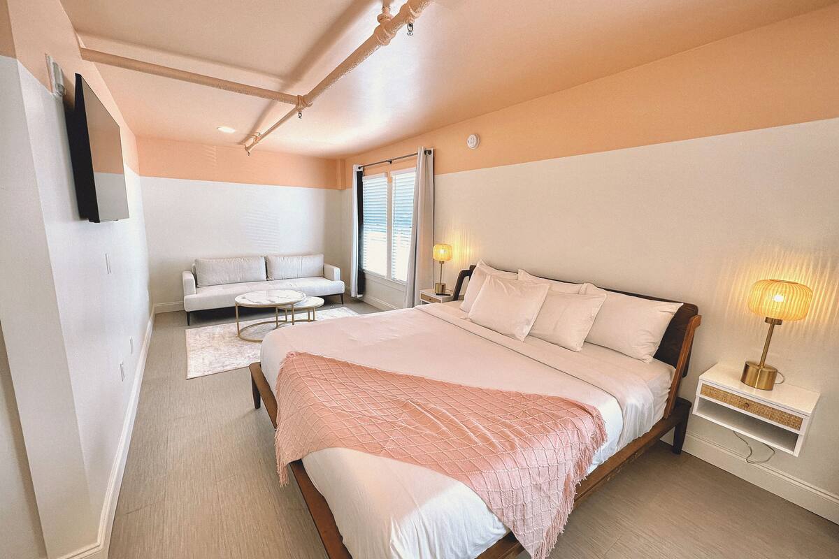 A bedroom with a large bed, a sofa, a small table, and a nightstand with a lamp.