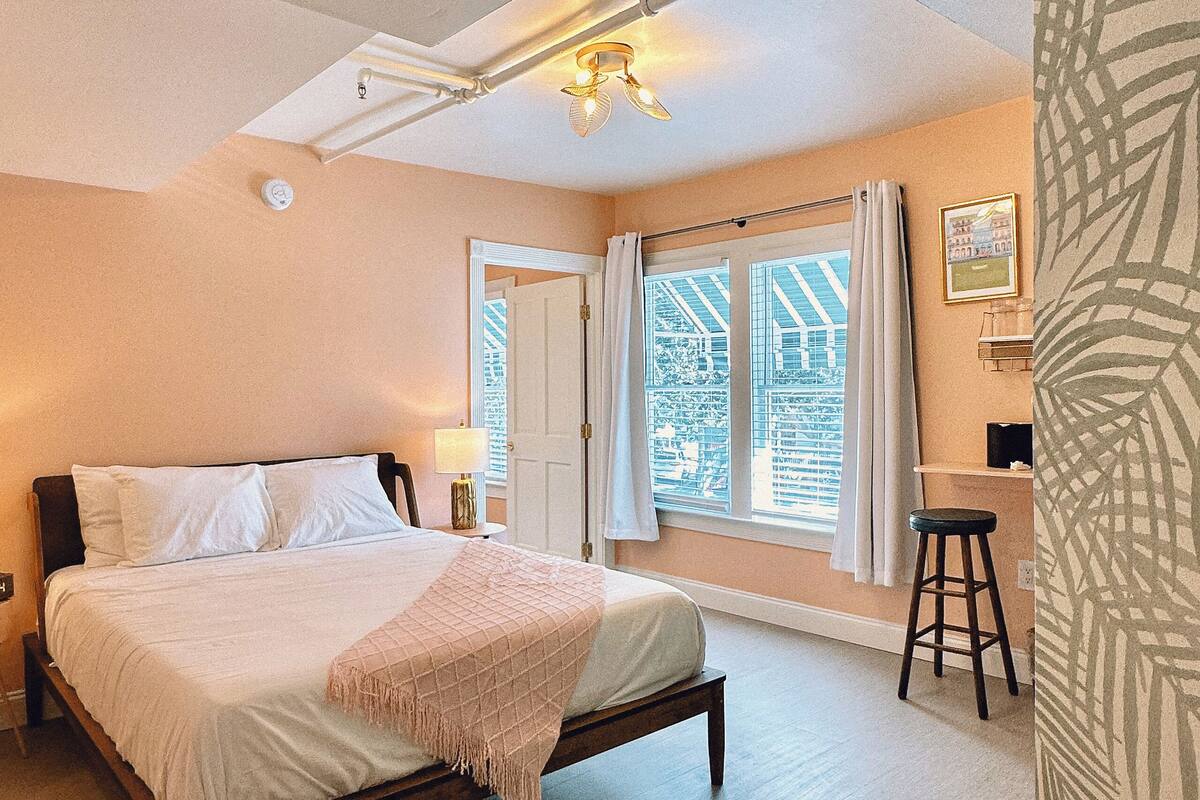 A bedroom with a bed, a window with curtains, a desk, and a chair.
