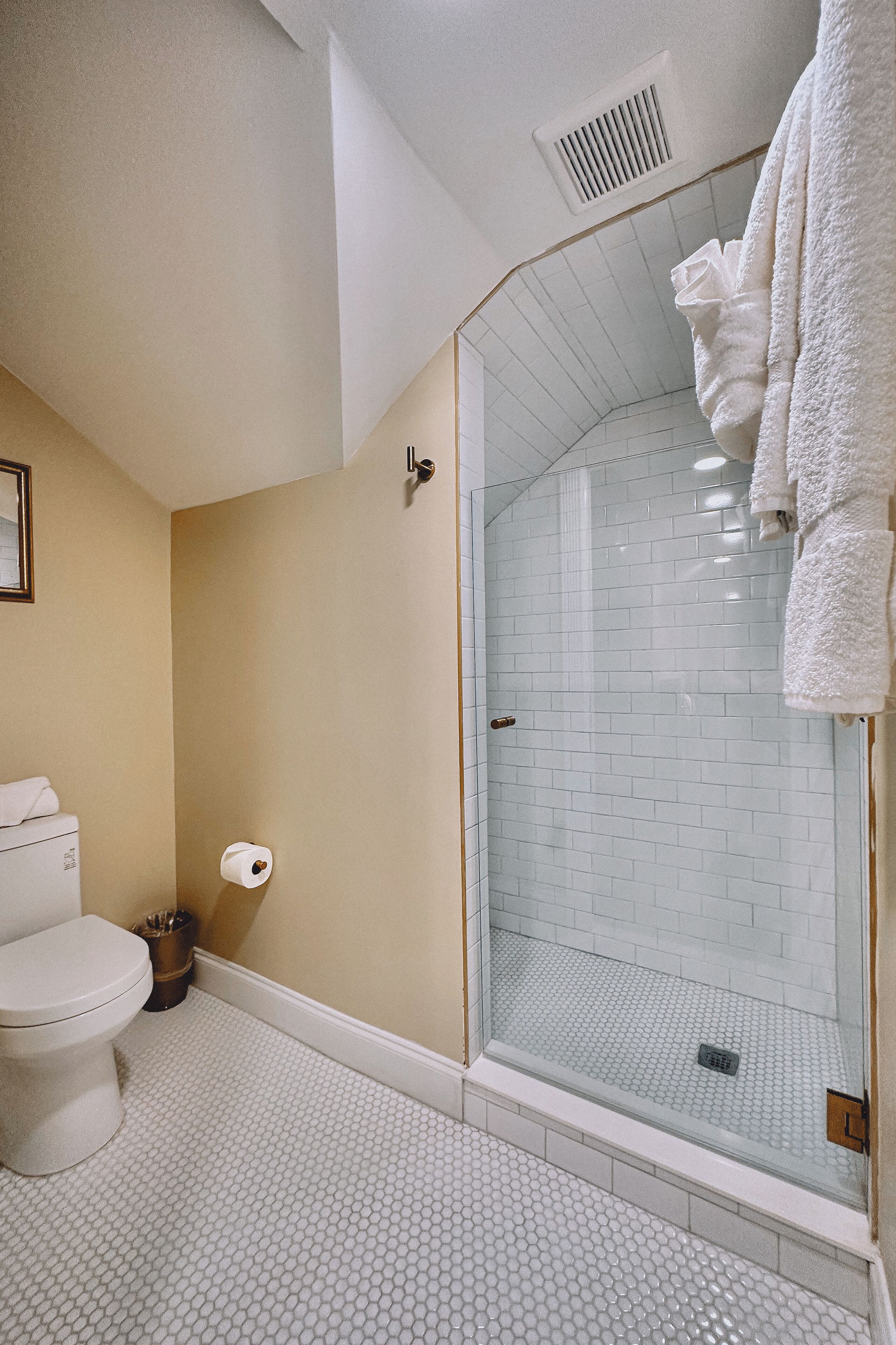 A bathroom with a toilet, a glass shower enclosure, and a white towel hanging on the wall.