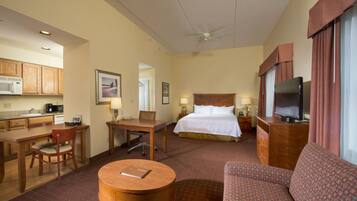 A hotel room with a bed, a TV, a sofa, a desk, a chair, and a small table.
