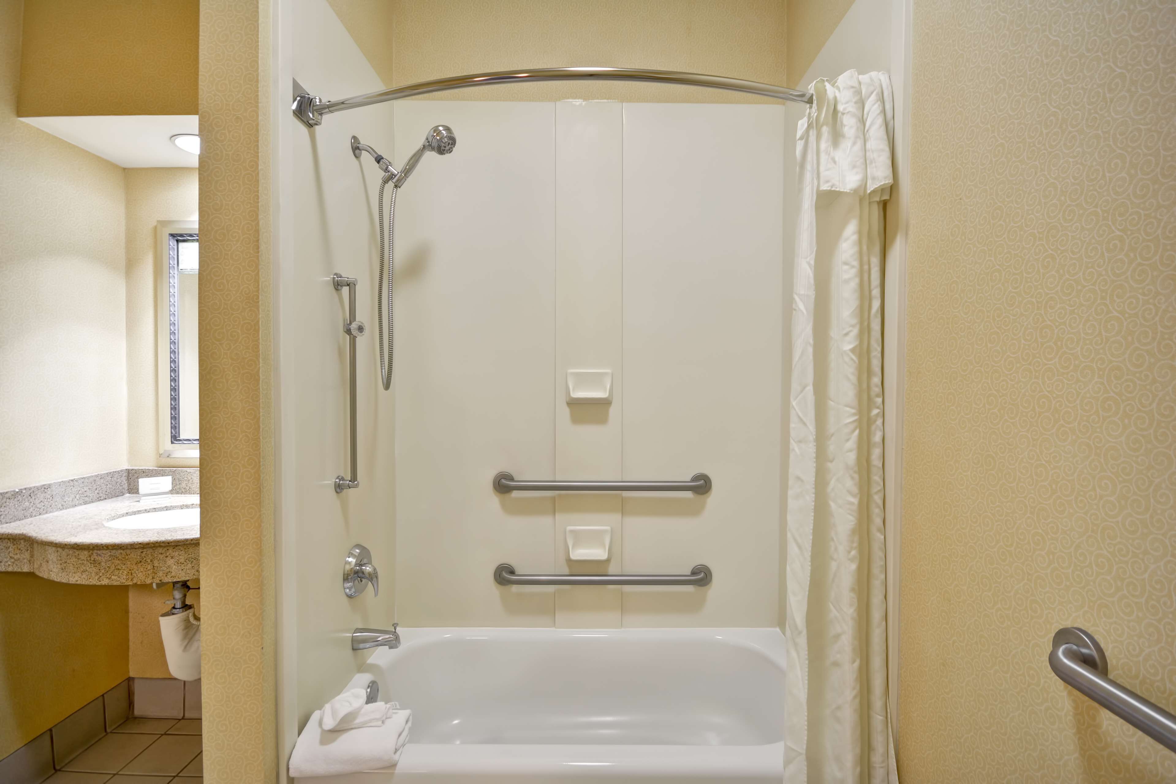 A bathroom with a shower, grab bars, a sink, and a toilet.
