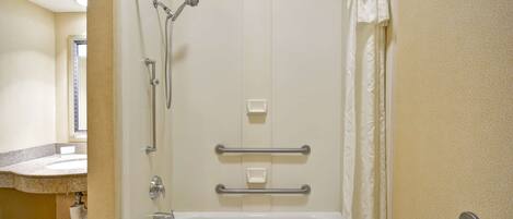 A bathroom with a shower, grab bars, a sink, and a toilet.