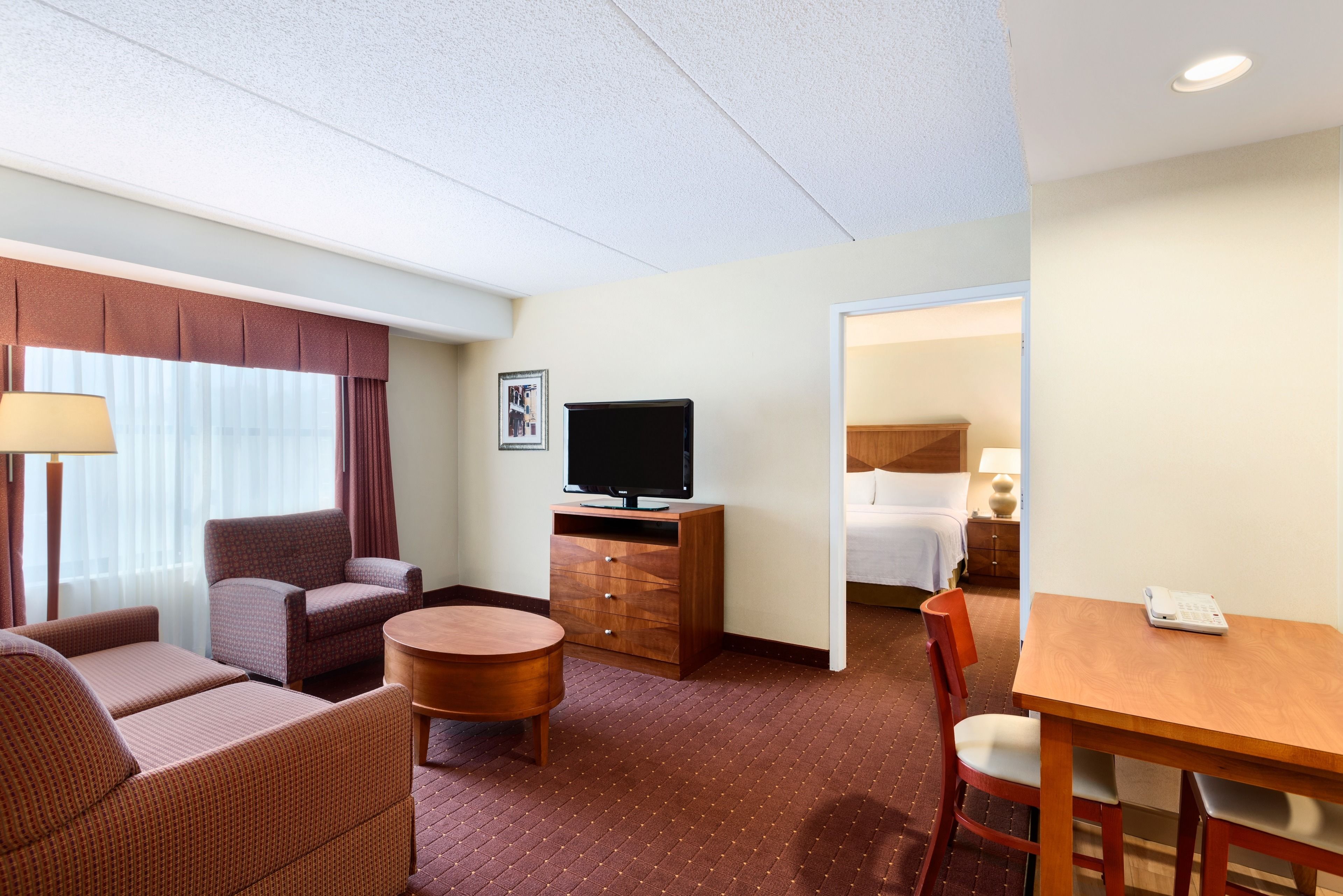 A hotel room with a sofa, armchair, TV, and a small dining table.