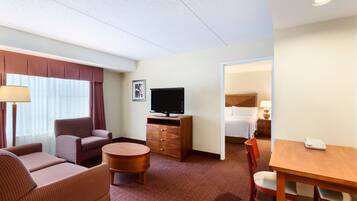 Habitación de hotel con sofá, sillón, televisor y una pequeña mesa de comedor.
