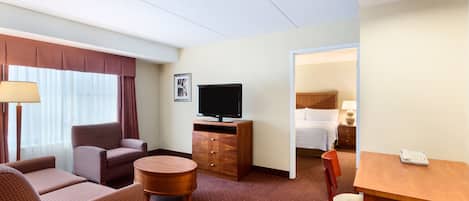A hotel room with a sofa, armchair, TV, and a small dining table.