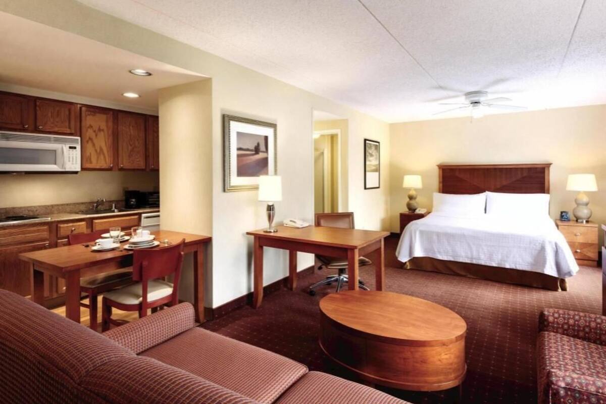 Habitación de hotel con cama, escritorio, mesa de comedor, sofá y área de cocina.