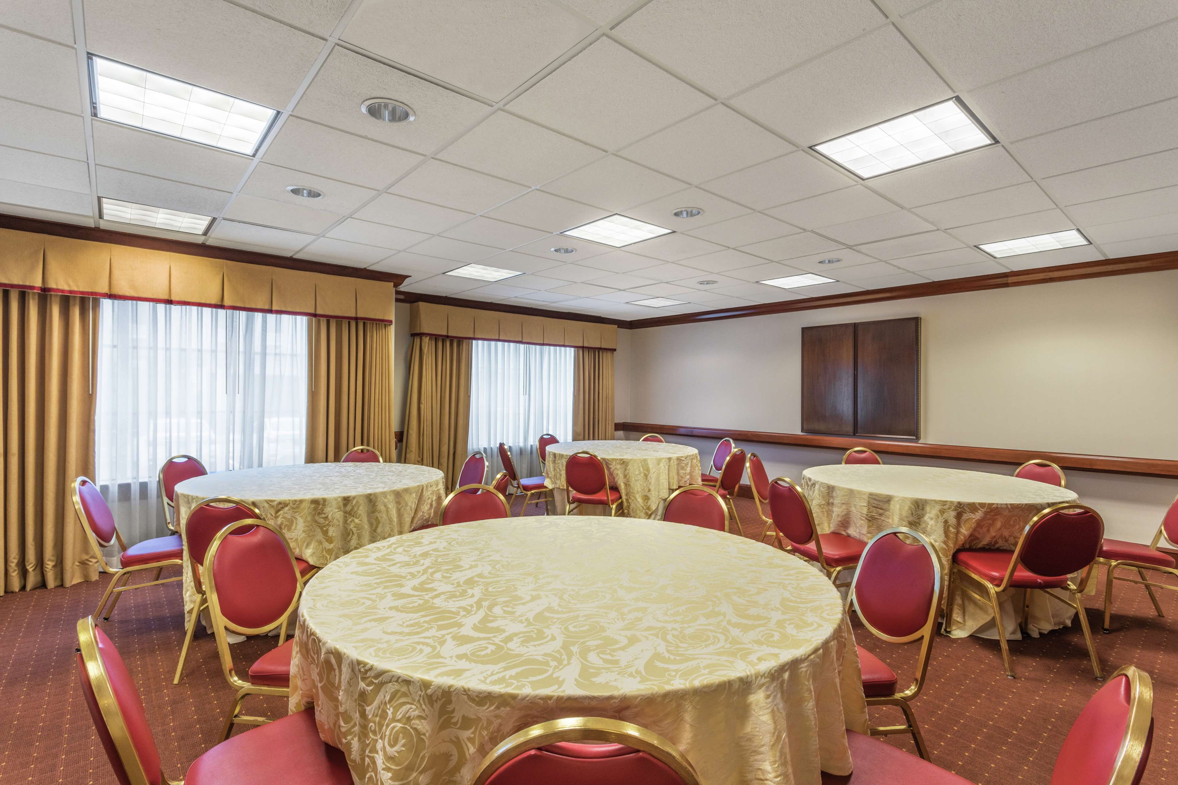 A conference room with multiple round tables, red chairs, and beige curtains.