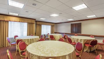 A conference room with multiple round tables, red chairs, and beige curtains.