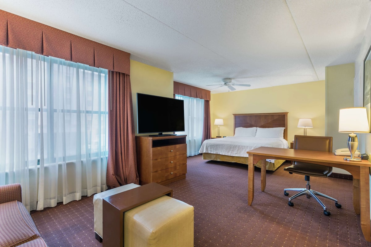 Habitación de hotel con cama, escritorio, silla, televisión y ventilador de techo.