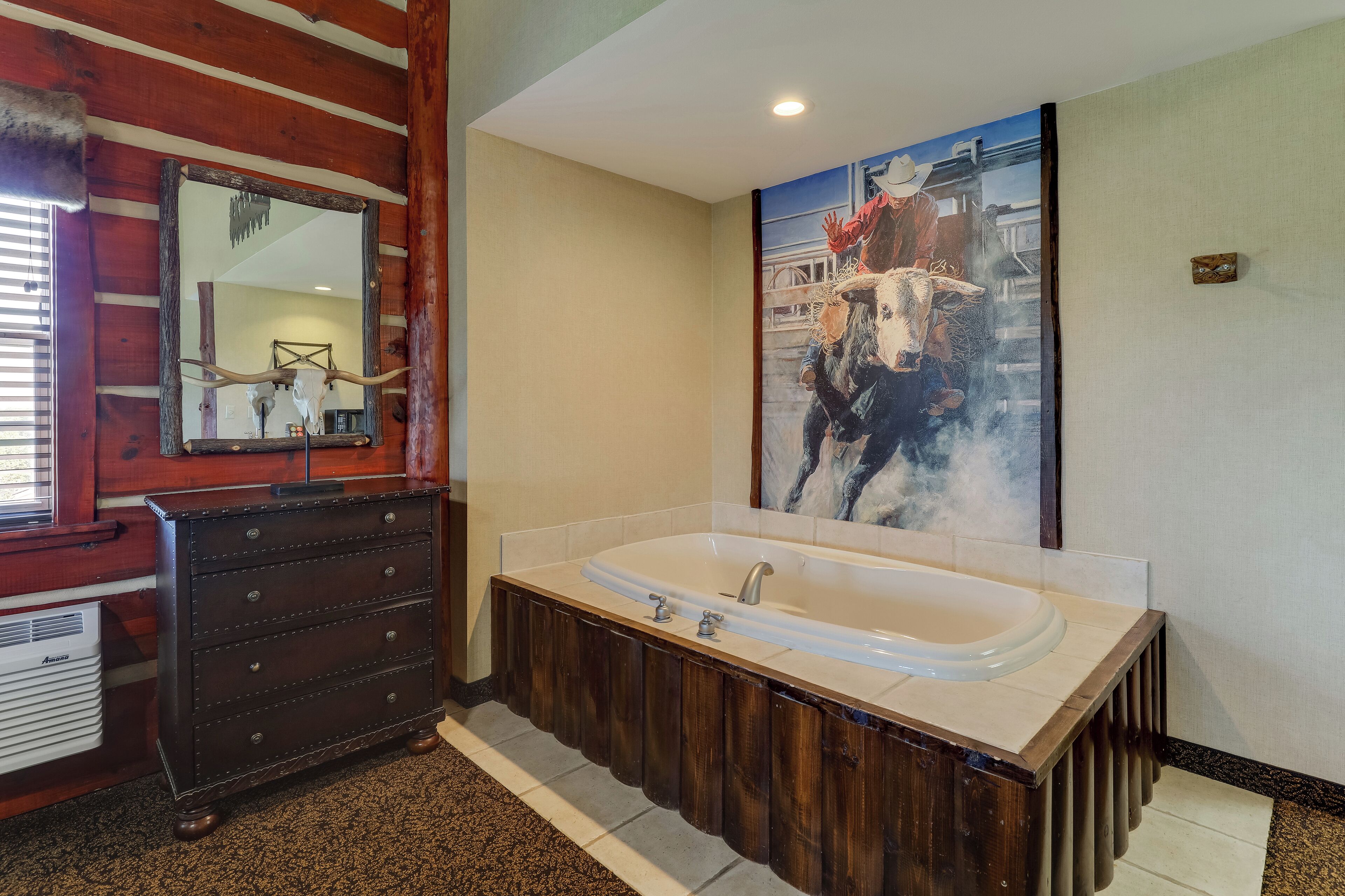 Een badkamer met een houten wastafel, een grote spiegel, een schilderij van een cowboy en een bad.