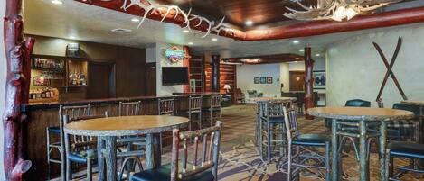 A rustic interior with wooden tables and chairs, a bar area, and a chandelier made from antlers.