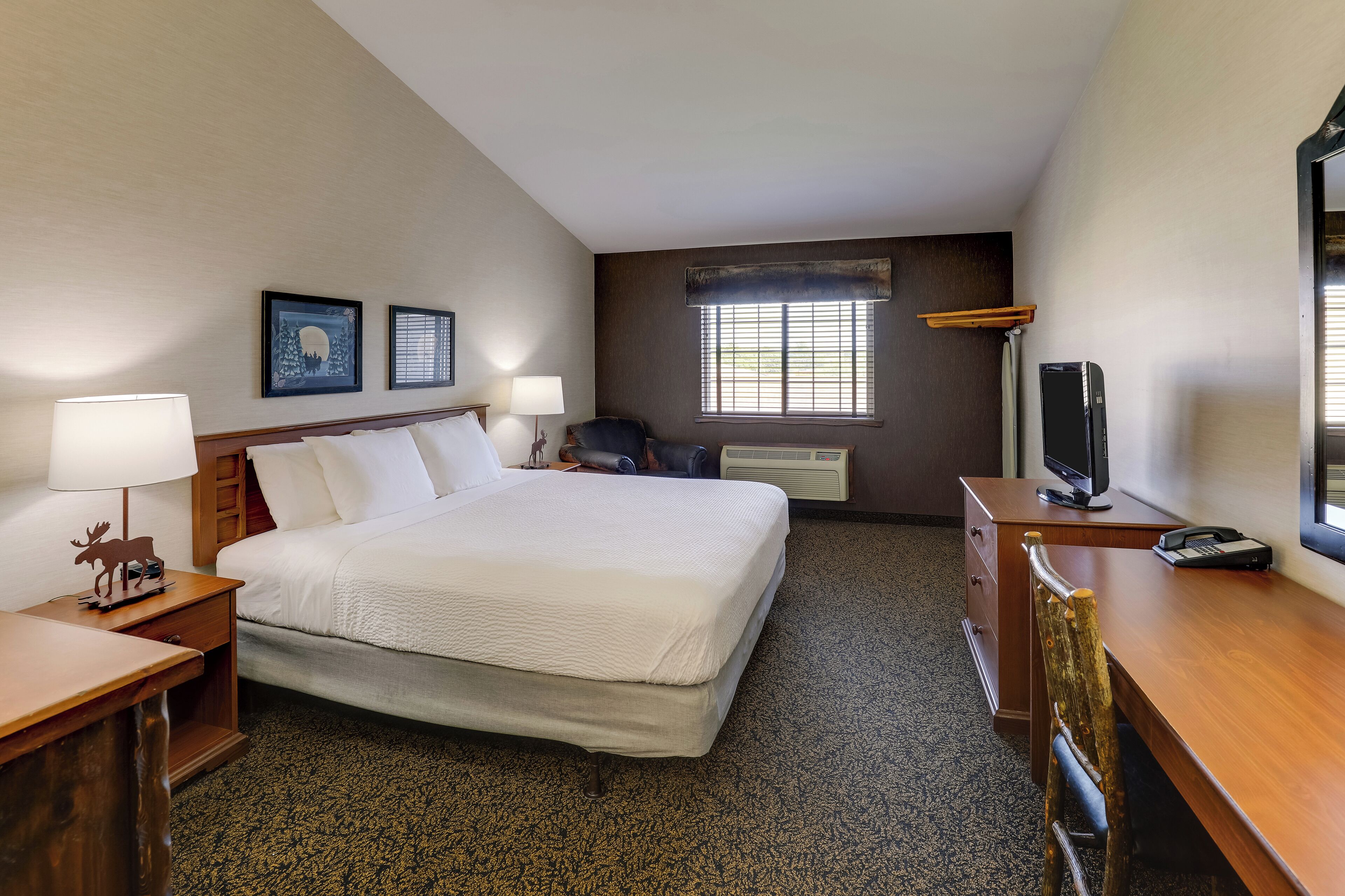 Een hotelkamer met een bed, een bureau met een computer, een televisie en twee aan de muur bevestigde fotolijstjes.