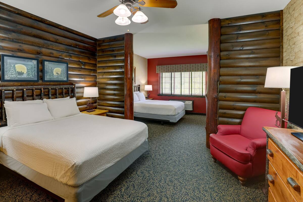 A log cabin-style room with a large bed, a red armchair, and a small desk.