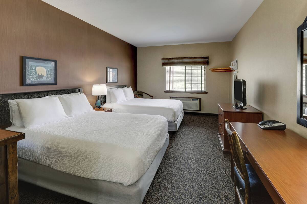A hotel room with two beds, a desk, a chair, a TV, and a window with blinds.