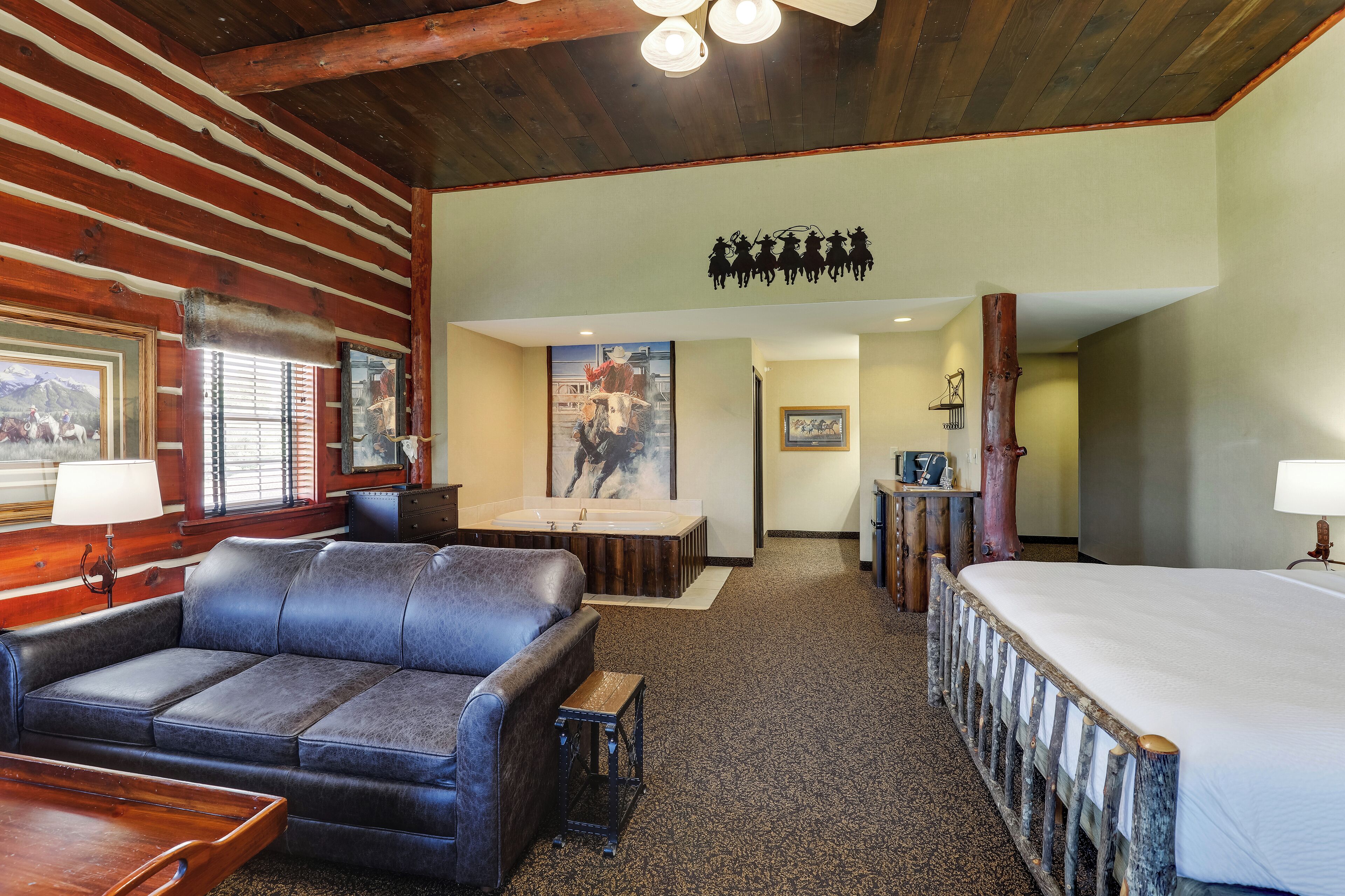 A log cabin-style room with a large bed, a sofa, a small table, a bathtub, and a wooden ceiling.