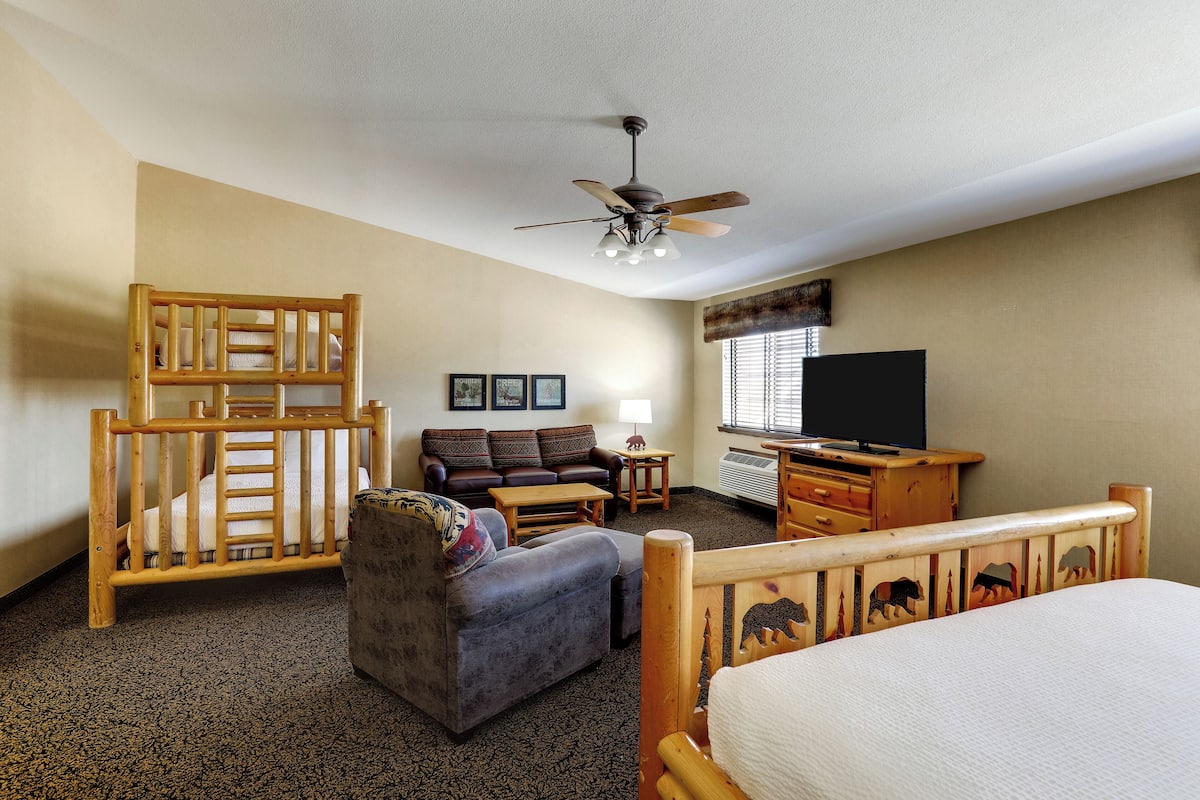 A room with a bed, a sofa, a chair, a desk, a television, and a ceiling fan.