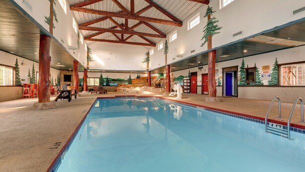 Una piscina interior con vigas de madera, paredes de piedra y árboles artificiales.