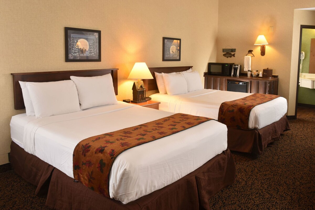 A hotel room with two beds, a nightstand, a lamp, a television, and a mirror.