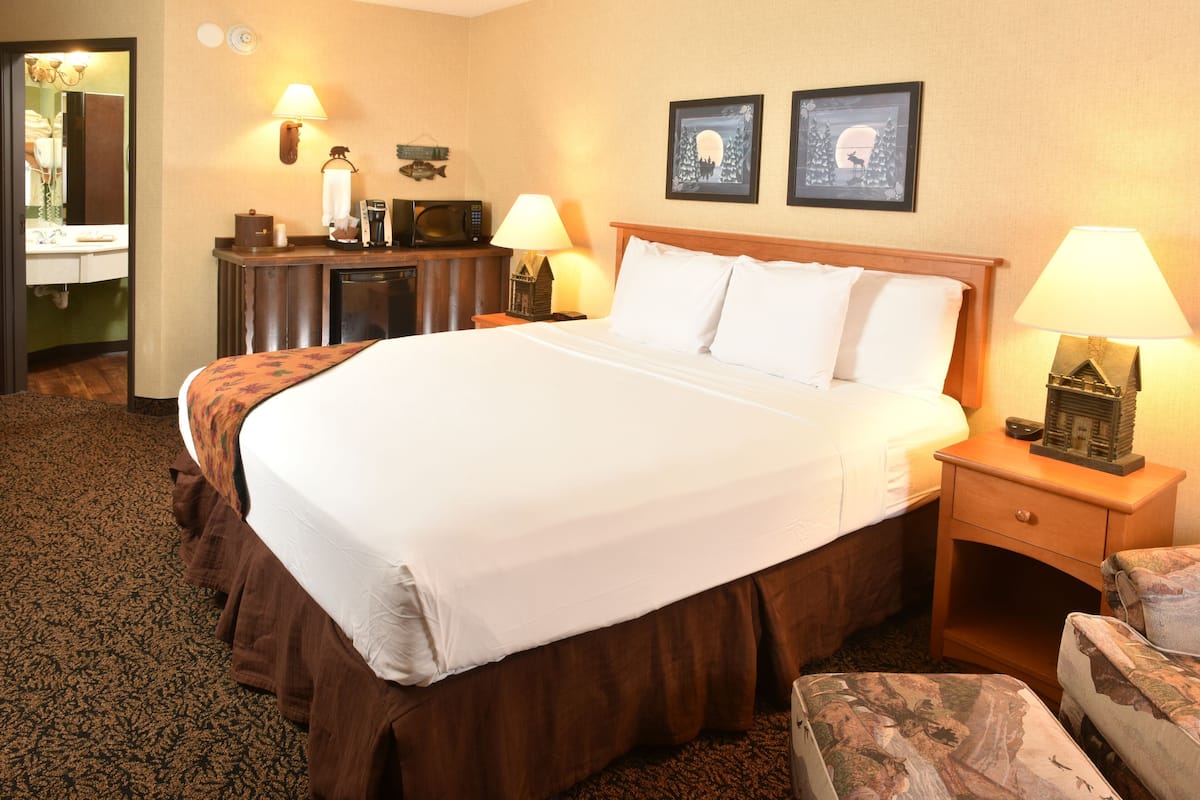 A hotel room with a large bed, a desk with a lamp, a chair, and two framed pictures on the wall.