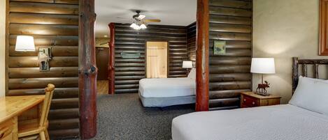A log cabin-style room with a bed, two smaller beds, a desk, and a chair.
